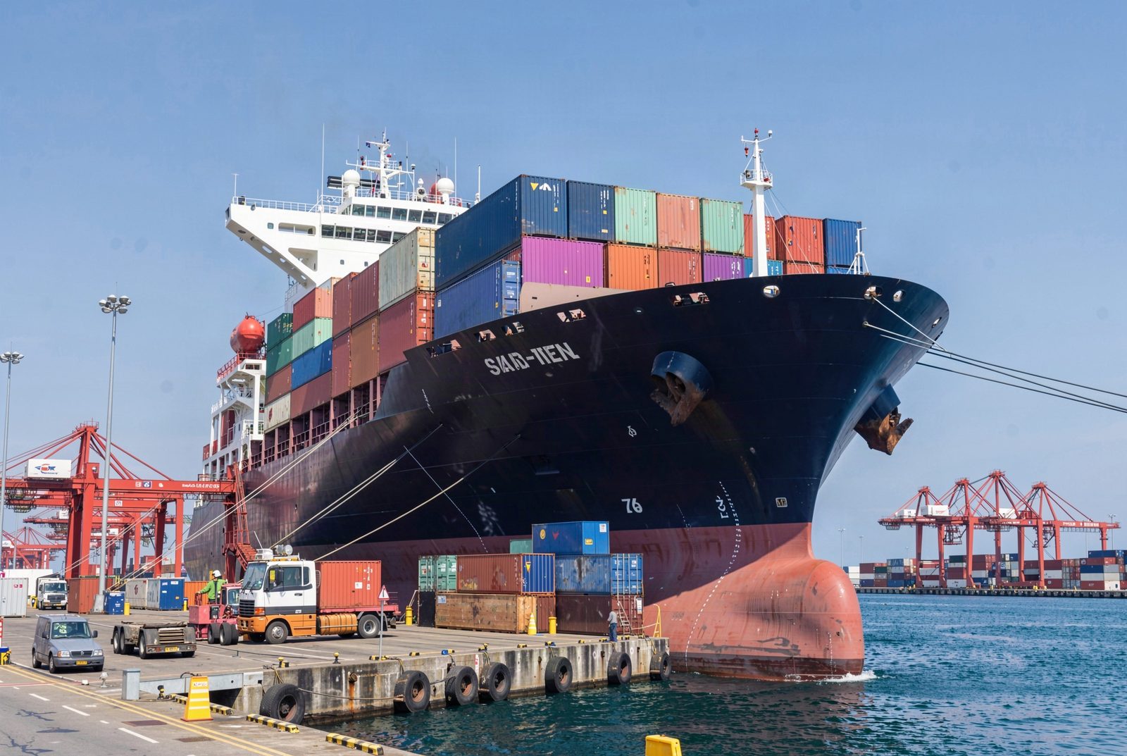 Buque de carga grande atracado en una terminal portuaria, con contenedores apilados y grúas pórtico bajo un cielo despejado